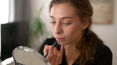 Makyaj yapan genç bir kadın, rahat bir odada oturan aynaya bakıyor. Güzel bir kadın kendini içeride güzelleştiriyor. Güzellik, makyaj konsepti.