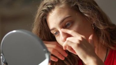 Güzellik ve doğallık kavramı. Genç bir kadın yüzündeki kızarıklıkları inceliyor. Aynaya bakarken tenine dokunuyor. Yüz bakımı. Sivilce.