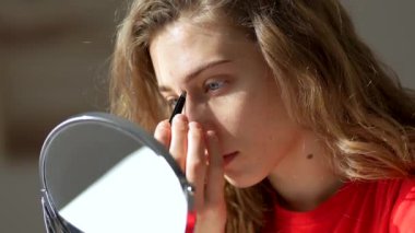 Güzel bir kadın sıcak bir odada aynaya bakarken kaşlarını cımbızla yoluyor. Genç bir kadın yüz bakımı yapıyor, içeride kaşlarını yoluyor. Güzellik konsepti, cilt bakımı.