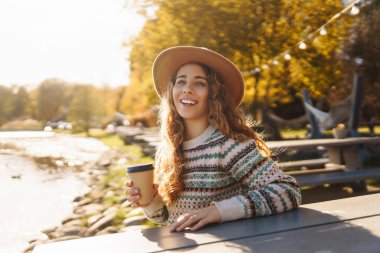 Nehrin kenarında oturan, elinde kahvesiyle genç bir kadın. Sonbahar Sabahı.