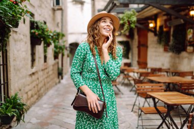 Mimari ve açık hava kafeleriyle süslenmiş güzel bir kasaba meydanında gezinen kıvırcık saçlı mutlu kadın. Avrupa şehri. Moda, yaşam tarzı konsepti
