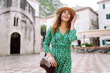 Mimari ve açık hava kafeleriyle süslenmiş güzel bir kasaba meydanında gezinen kıvırcık saçlı mutlu kadın. Avrupa şehri. Moda, yaşam tarzı konsepti