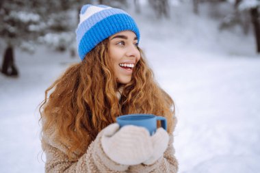 Karlı bir ormanda termosla mutlu bir kadın doğanın tadını çıkarıyor. Sıcak bir içki ve romantik bir seyahatin tadını çıkarıyor. Seyahat, turizm, doğa, aktif yaşam tarzı.