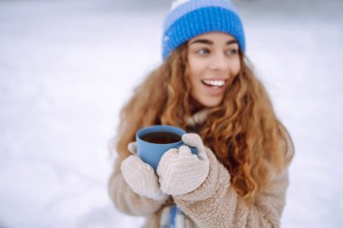 Karlı bir ormanda termosla mutlu bir kadın doğanın tadını çıkarıyor. Sıcak bir içki ve romantik bir seyahatin tadını çıkarıyor. Seyahat, turizm, doğa, aktif yaşam tarzı.