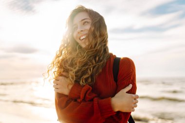 O, plaj boyunca yürürken, kadın turist sırt çantasını ayarladı, tuzlu deniz havasını ve gün batımında dalgaların sesini içine aldı. Sakinlik ve sükunet. Seyahat, turizm konsepti.