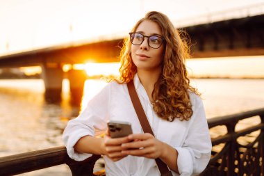 Duvarda oturan genç bir kadın, zaman geçirmek için telefonunu karıştırıyor. Tatil kavramı, teknoloji, blog kavramı.