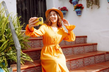 Genç bir kadın güneşli bir köye yaptığı gezinin hatırası olarak çabucak bir selfie çekecek. Turist Macerası. Seyahat, teknoloji, blog yazma.