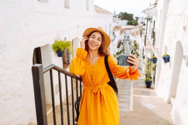 Genç bir kadın güneşli bir köye yaptığı gezinin hatırası olarak çabucak bir selfie çekecek. Turist Macerası. Seyahat, teknoloji, blog yazma.