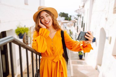 Genç bir kadın güneşli bir köye yaptığı gezinin hatırası olarak çabucak bir selfie çekecek. Turist Macerası. Seyahat, teknoloji, blog yazma.