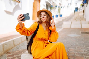 Genç bir kadın güneşli bir köye yaptığı gezinin hatırası olarak çabucak bir selfie çekecek. Turist Macerası. Seyahat, teknoloji, blog yazma.