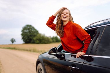 Mutlu kadın dinleniyor ve araba penceresinden dışarı çıkmanın tadını çıkarıyor. Araba Macerası. Seyahat, turizm, doğa, aktif yaşam
