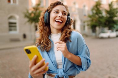 Şehir caddesinde yürüyen ve güzel müzik dinleyen bir kadın. Seyahat, turizm, teknoloji, blog konsepti.