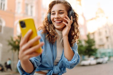 Şehir caddesinde yürüyen ve güzel müzik dinleyen bir kadın. Seyahat, turizm, teknoloji, blog konsepti.