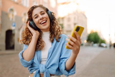 Şehir caddesinde yürüyen ve güzel müzik dinleyen bir kadın. Seyahat, turizm, teknoloji, blog konsepti.