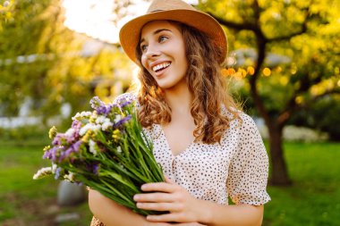 Mutlu kadın, elinde taze koparılmış kır çiçekleri buketi ile parkta dolaştı. Moda tarzı.