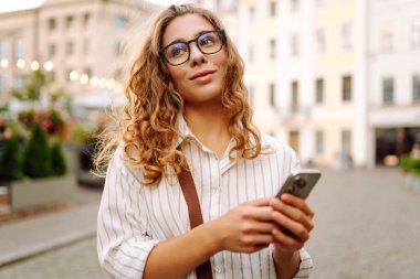 Sokakta akıllı telefon kullanan kendine güvenen genç bir turist. Teknoloji, blog yazma, iletişim kavramı.