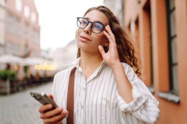 Sokakta akıllı telefon kullanan kendine güvenen genç bir turist. Teknoloji, blog yazma, iletişim kavramı.