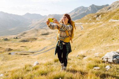 Bir kadın elinde telefonla kayalık arazide duruyor. Önünde nefes kesici manzaranın fotoğrafını çekiyor. Doğa özgürlüğü macerası, mutlu tatiller. Günlük tutma.