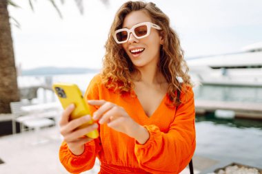 Sokakta elinde telefonla yürüyen genç bir kadın. Başlarken bağlandı. Palmiye ağaçları. Harika bir sokak.