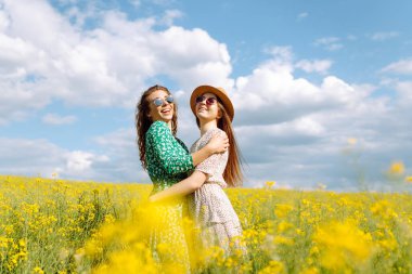 Çiçek tarlasında yürüyen iki güzel kadın. Doğa, tatil, rahatlama ve yaşam tarzı. Yaz manzarası.