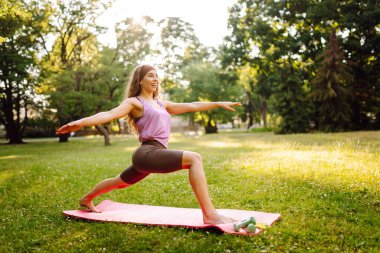 Genç sıska kadın halka açık parkta esneme ya da yoga gevşeme egzersizi yapıyor. Yaşam tarzı ve meditasyon konsepti.