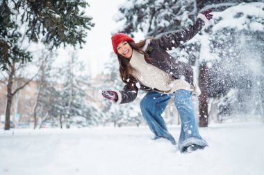Genç bir kadın kış günü parkta karla eğleniyor. Eğlence, rahatlama, kış tatili kavramı.