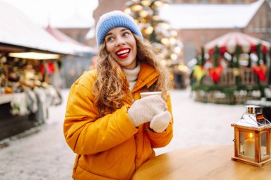 Mutlu kadın Noel pazarında sıcak bir içecek içer. Şenlik ışıklarıyla süslenmiştir. Noel festivali, kış tatili konsepti..