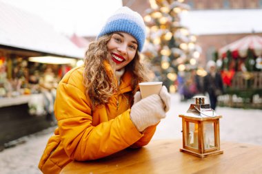 Mutlu kadın Noel pazarında sıcak bir içecek içer. Şenlik ışıklarıyla süslenmiştir. Noel festivali, kış tatili konsepti..