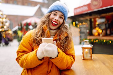 Mutlu kadın Noel pazarında sıcak bir içecek içer. Şenlik ışıklarıyla süslenmiştir. Noel festivali, kış tatili konsepti..