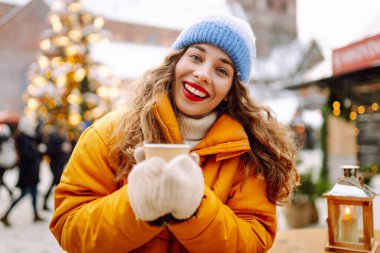 Mutlu kadın Noel pazarında sıcak bir içecek içer. Şenlik ışıklarıyla süslenmiştir. Noel festivali, kış tatili konsepti..