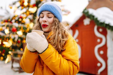 Mutlu kadın Noel pazarında sıcak bir içecek içer. Şenlik ışıklarıyla süslenmiştir. Noel festivali, kış tatili konsepti..