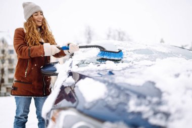 Genç bir kadın kar fırtınasından sonra arabasını fırçayla temizliyor. Soğuk kış havasında araba sahiplerinin sorunları.