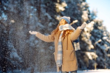 Genç bir kadın eğleniyor, kışın karlı bir parkta yürüyor. İnsanlar, mevsim ve Noel konsepti.
