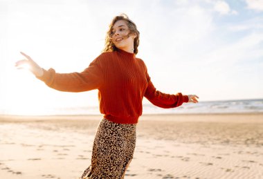 Rüzgarlı bir günde güzel bir kadın kumsal boyunca yürür ve sonbahar havasının tadını çıkarır. Seyahat, hafta sonu, rahatlama ve yaşam tarzı konsepti.