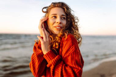 Rüzgarlı bir günde güzel bir kadın kumsal boyunca yürür ve sonbahar havasının tadını çıkarır. Seyahat, hafta sonu, rahatlama ve yaşam tarzı konsepti.