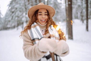 Elinde pırıltılarla mutlu bir kadın kar ormanında kış tatilinin tadını çıkarıyor. Noel, yeni yıl.