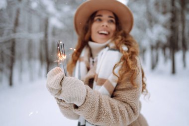 Elinde pırıltılarla mutlu bir kadın kar ormanında kış tatilinin tadını çıkarıyor. Noel, yeni yıl.