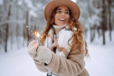 Elinde pırıltılarla mutlu bir kadın kar ormanında kış tatilinin tadını çıkarıyor. Noel, yeni yıl.