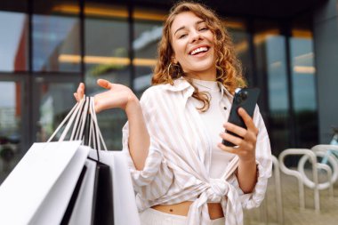 Alışveriş çantalı ve cep telefonu kullanan bir kadın. İnternetten alışveriş konsepti. Satılık. Kara Cuma. Satış ekommerce uygulaması.