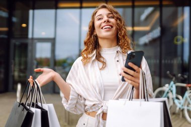 Alışveriş çantalı ve cep telefonu kullanan bir kadın. İnternetten alışveriş konsepti. Satılık. Kara Cuma. Satış ekommerce uygulaması.