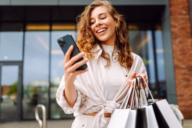 Alışveriş çantalı ve cep telefonu kullanan bir kadın. İnternetten alışveriş konsepti. Satılık. Kara Cuma. Satış ekommerce uygulaması.