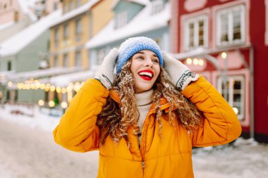 Genç kadın turist, parlak çelenklerle süslenmiş kış caddelerinde yürüyor. Kış tatili Noel Fuarı.