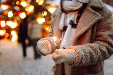 Noel parıltılarını ellerinle kapat. Soğuk kış akşamında Noel pazarında elinde yanan maytap tutan genç bir kadın. Noel, yeni yıl.