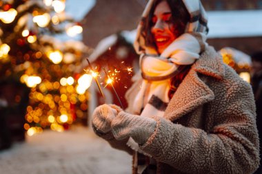 Noel parıltılarını ellerinle kapat. Soğuk kış akşamında Noel pazarında elinde yanan maytap tutan genç bir kadın. Noel, yeni yıl.