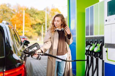 Benzin istasyonunda arabasını benzinle dolduran güzel bir kadın. Çevrimiçi ödeme. Kadın, telefonundaki uygulamayı kullanarak benzin istasyonunun parasını ödüyor..