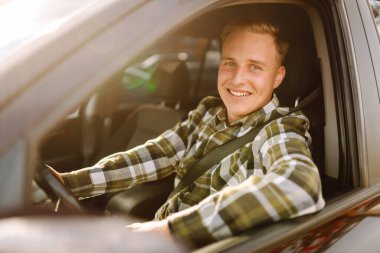 Arabada gülümseyen ve kameraya bakan genç bir adam. Bir araba alıp kiralamak. Araba yolculuğu, yaşam tarzı konsepti..