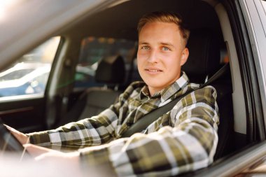 Arabada gülümseyen ve kameraya bakan genç bir adam. Bir araba alıp kiralamak. Araba yolculuğu, yaşam tarzı konsepti..