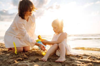 Anne ve kızı sahilde eğleniyor. Oyuncak oynuyor. Aile tatili.