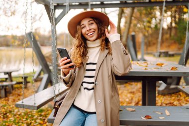 Güzel bayan gezgin piknik masasında oturuyor ve cep telefonuyla yazı yazıyor. Sonbahar Sabahı.