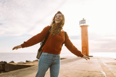 Canlı kırmızı bir deniz fenerinin yanında yürüyen mutlu bir turist. Doğanın tadını çıkarıyorum. Seyahat, hafta sonu, rahatlama ve yaşam tarzı konsepti.